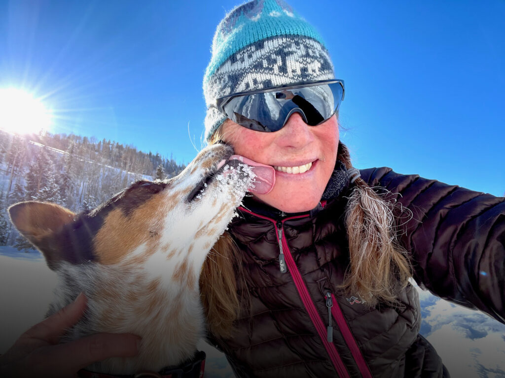 Darcy in a snowy field with a speckled cattle dog, and snow dusted hills in the background under a soft purple sky.